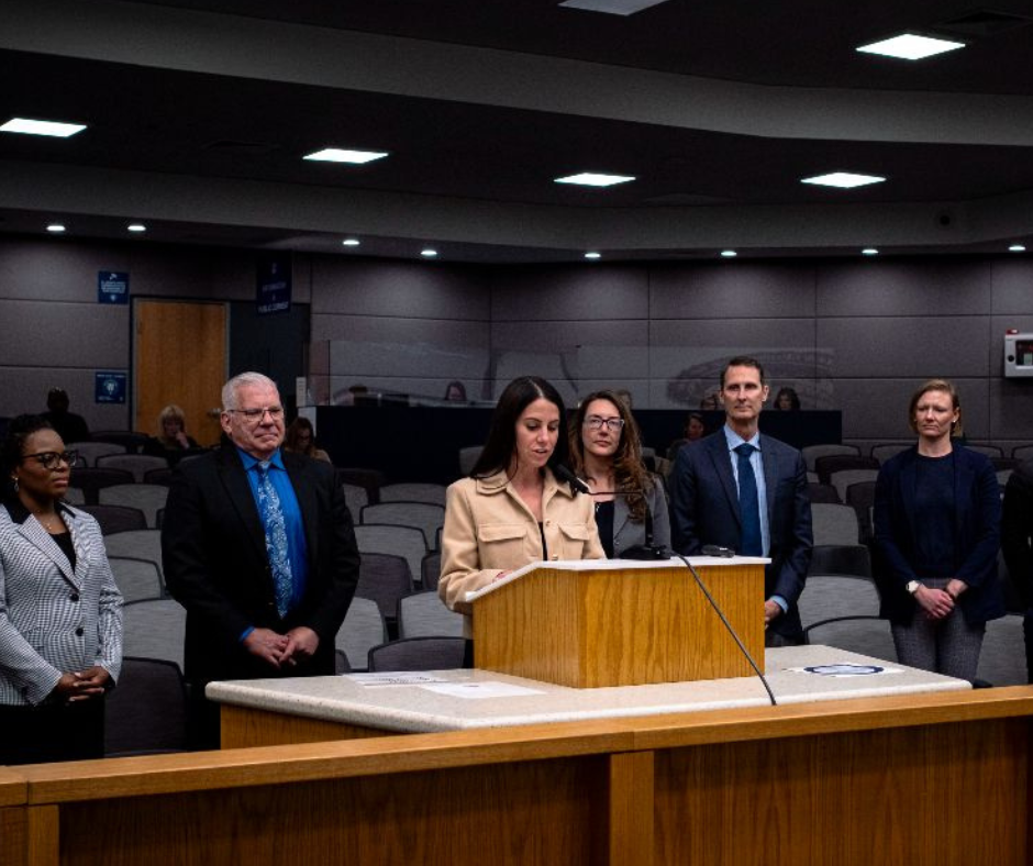 Group of people in a conference room giving speech; woman speaking into microphone